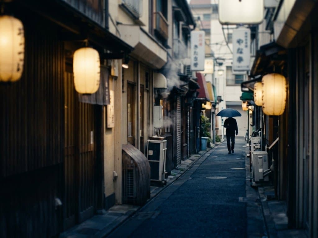 A narrow Tokyo alley at dusk, paper lanterns glowing against deep blue twilight